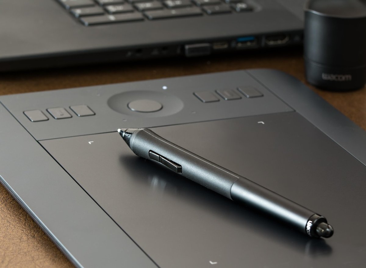 Graphics drawing tablet with a stylus resting on it beside a laptop keyboard
